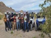 A group of people wearing helmets and gloves stand in front of two off-road vehicles in a rocky desert landscape.
