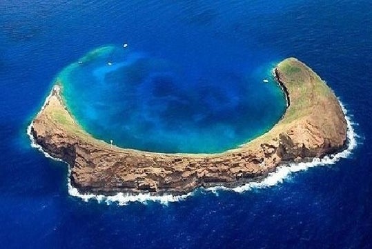 An aerial view of the crescent-shaped Molokini crater in a sea of blue.