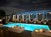 A rooftop pool at night with lit lounge chairs and city skyline views in the background.