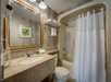 Bathroom with a granite countertop, wall-mounted hairdryer, towel rack, shower-tub combo with a white curtain, and framed leaf artwork.