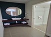 Modern bathroom with a round mirror above a sink, open shelf with rolled towels, and a walk-in glass shower visible to the right.