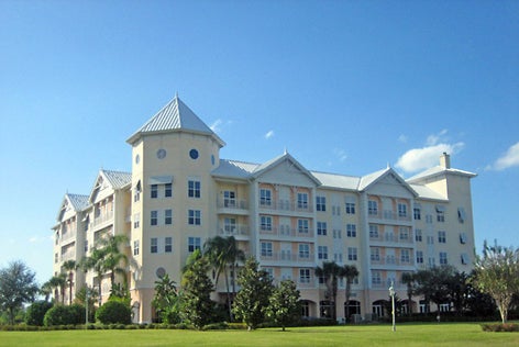 A multi-story building with a turret, surrounded by palm trees and grass, under a clear blue sky.