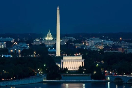 Nighttime view of the National Mall in Washington, D.C., featuring the Lincoln Memorial, Washington Monument, and U.S. Capitol building illuminated against a dark sky.