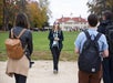 A tour guide speaks to a group of people outdoors, with a historic building and autumn trees visible in the background.