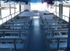 Rows of empty metal benches on a covered open-air boat, with life preservers and a view of water and shoreline in the background.