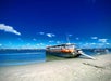 A large tour boat with an American flag is docked on a sandy beach under a clear blue sky, with calm water and another boat in the background.