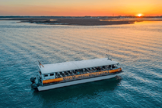 The Explorer cruise boat full of passengers in the water during sunset with land in the distance near Myrtle beach.