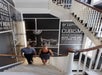 Two people walk up a staircase with white railings, surrounded by black-and-white wall graphics featuring text and a large clock image.