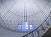 LED light rods hang from the ceiling above a spiral staircase with a large window in the background, creating a geometric and luminous installation.