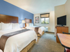 Hotel room with two double beds, wooden headboards, a TV on a stand, a window with a blind, and a small table with a chair. The walls are painted blue and white.