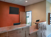 Empty hotel reception desk with a wood counter, a blank TV screen on the wall, an open door, and a small air conditioning unit visible through a window.