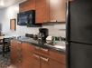 A kitchenette with brown cabinets, a stove, microwave, coffee machine, sink, and refrigerator in a room at the My Place Hotel-Shakopee.