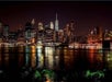 Night view of a brightly lit city skyline reflecting on a body of water, featuring tall buildings and a bridge on the right.