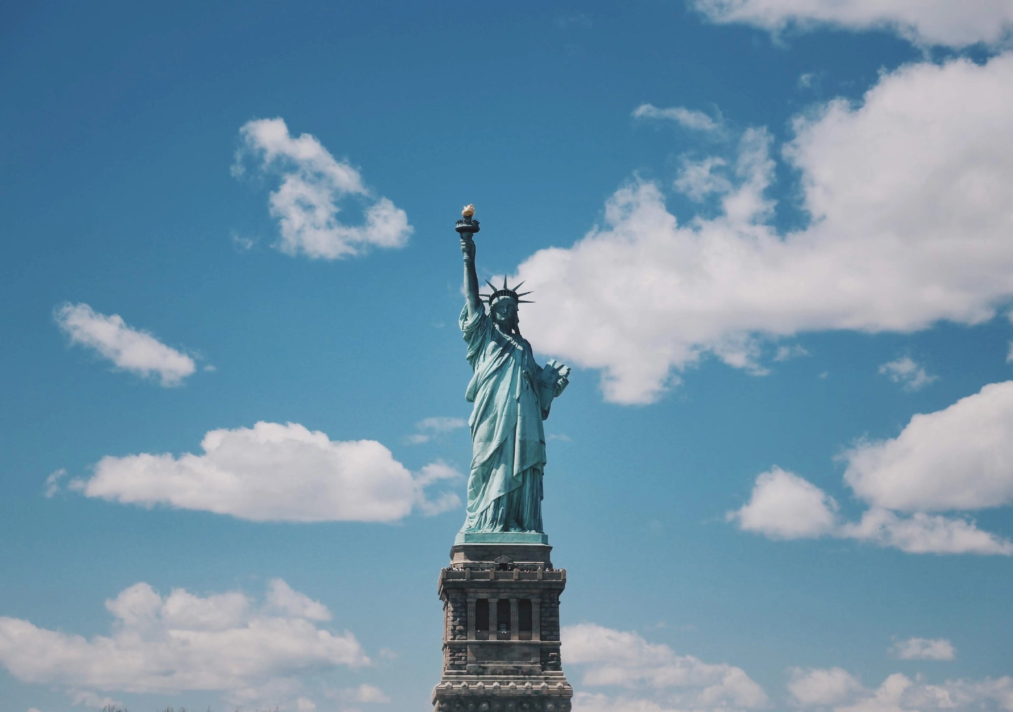 The Statue of Liberty stands against a blue sky with scattered white clouds.