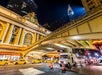 Nighttime street scene in New York City showing Grand Central Terminal, yellow taxis, a bridge, and the Chrysler Building in the background.