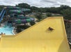 A person rides an inflatable tube down a steep yellow water slide at a water park, with a winding purple and green slide visible in the background.