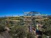 A large outdoor ropes course with multiple levels, climbing structures, and obstacles is surrounded by trees under a clear blue sky.