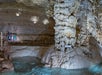 A group of visitors exploring the stunning formations inside a cavern, characterized by large stalagmites and a reflective pool of water, with a sign indicating "The Watchtower."