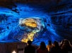 A view of the cave interior bathed in blue and gold lighting, where visitors gaze at the illuminated rock formations and the cavern's depth.