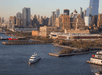 Aerial view of a white cruise boat sailing through the water in the evening with New York City in the distance.