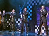 The men wear black suits while singing during the show