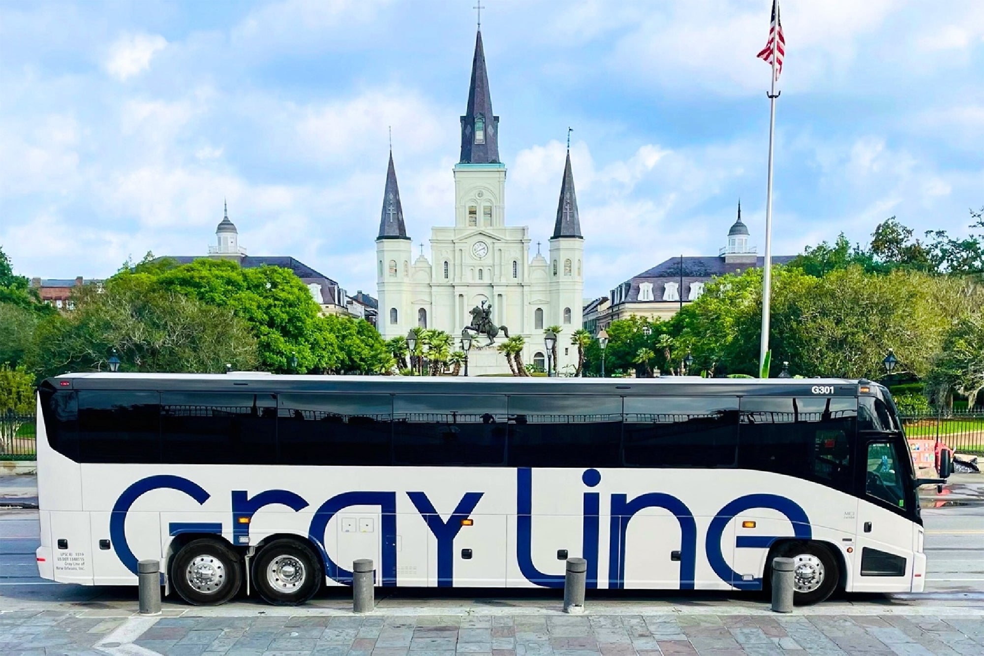 A Gray Line tour bus is parked in front of Jackson Square, with St. Louis Cathedral and surrounding buildings visible in the background.