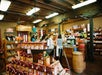 A group of people stands at the counter of a rustic store filled with shelves of snacks, souvenirs, and various products under exposed wooden beams.