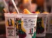 Plastic cups featuring "The Court of Two Sisters New Orleans" logo, filled with drinks, fruit garnishes, and straws, are grouped together.