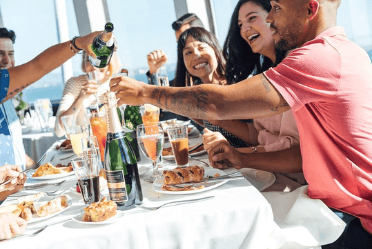 A group of friends laughing and smiling while having brunch on a bright and sunny day on the New York Brunch Cruise Pier 15.