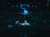 A packed crowd watches a basketball game at Barclays Center, with a large screen displaying graphics above the brightly lit court.