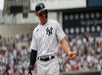 A Yankees players in a white and black uniform smiling and pointing out with one of his hands with a crowd in the stands behind him.
