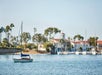 A lone sail boat sitting in the water with a marina full of boats behind it on a sunny day in Newport Beach, California.