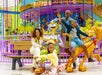 A family of four poses and smiles in front of a colorful carousel with cartoonish animal figures at an indoor amusement park.