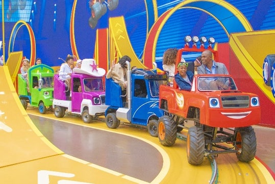People enjoying a ride in colorful, cartoon-themed mini trucks on a track with loop designs inside an amusement park.