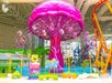 Vibrant indoor amusement ride shaped like a giant pink jellyfish with seats. Features a smiling cartoon character and colorful decor.