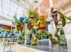 Four Teenage Mutant Ninja Turtles mascots pose on a stage in a bright indoor setting with a Nickelodeon Universe sign in the background.