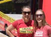 Two women wearing sunglasses and "Chicago Crime Tours" shirts stand smiling in front of a red and white tour bus.