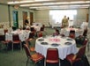 A room with round tables set with white cloths and black plates. Three people are setting up the tables.