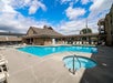 Outdoor swimming pool area with a small hot tub, surrounded by lounge chairs and a building under a partly cloudy sky.