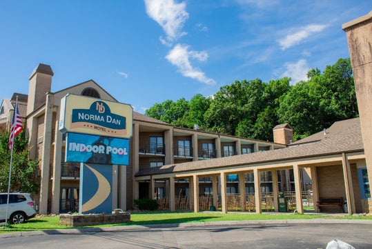 Exterior view of Norma Dan Motel with a prominent sign advertising an indoor pool, surrounded by greenery under a clear blue sky.