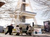 Four people sit at a table outdoors near the base of the Space Needle in Seattle, while a police officer stands nearby on a sunny day.