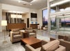A modern hotel lobby with beige seating, a wooden reception desk, computer stations, and large glass doors showing an outdoor view.
