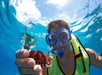 A person wearing a snorkel mask and life vest holds a sea urchin underwater while snorkeling in clear blue water.