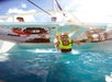Child in a yellow life vest and snorkel jumps into clear blue water from a boat, while others watch from above.