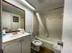 Small bathroom with a white bathtub-shower combo, toilet, and sink. A mirror hangs above the vanity. The shower curtain is partly pulled. Overhead lighting illuminates the space.