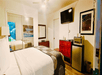 A hotel room with a white king bed, dresser, mini fridge, mirrored closet doors, and a TV mounted to the wall.