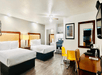 A hotel room with two queen beds, a desk and chair, small table with yellow chairs, and a small kitchen area.