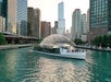 Tour boat with water fountain feature on Chicago River, surrounded by tall buildings in the cityscape.