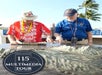 Two elderly men examine an outdoor 3D map display; one wears a red Hawaiian shirt and hat, the other a blue shirt and cap. A "115 Multimedia Tour" badge appears in the foreground.