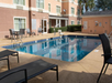 Outdoor swimming pool surrounded by lounge chairs and tables, located near a building with multiple windows.